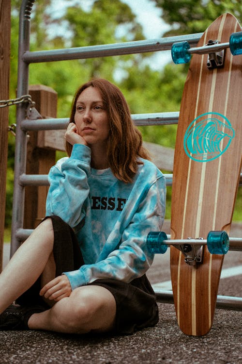 Free Woman in Teal and Black Crew Neck T-shirt Sitting on Brown Wooden Bench Stock Photo