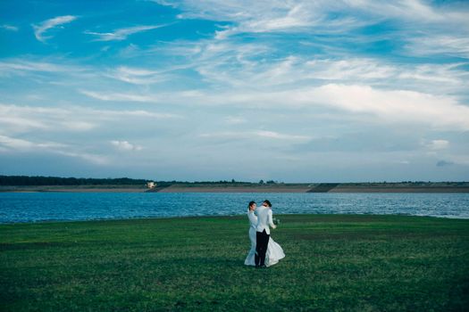 A couple in wedding attire celebrates their marriage near a scenic body of water.