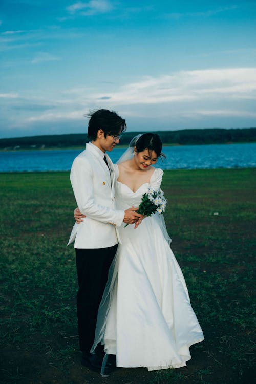 Man in White Suit Jacket and Woman in Wedding Dress on Grass Field 