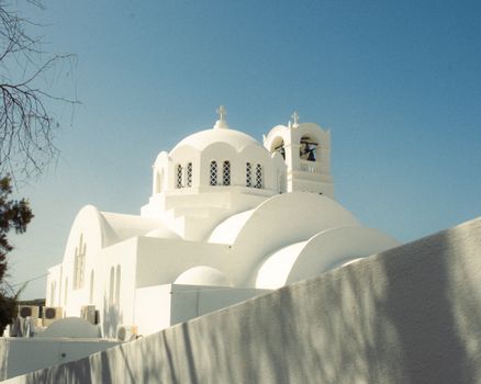 A striking white-domed church against a clear blue sky in Santorini, Greece, showcasing classic Cycladic architecture.