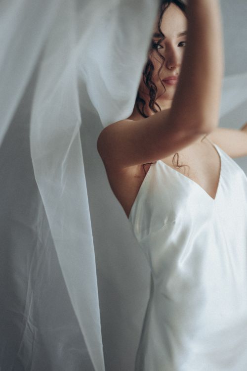 Free Bride in a satin wedding gown with a veil, elegantly posing indoors. Stock Photo