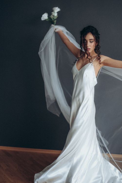 Free A beautiful bride in a white dress gracefully poses with a flowing veil and white roses. Stock Photo