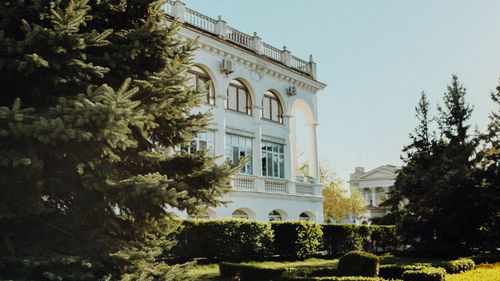 Free White classical building surrounded by lush evergreen trees under a clear sky, exuding historic charm. Stock Photo