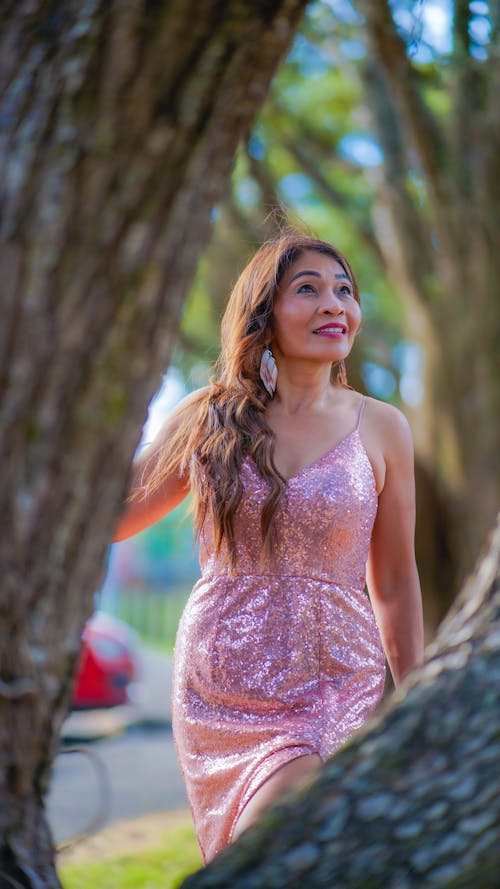A Woman in Pink Dress Standing Near the Tree Trunk