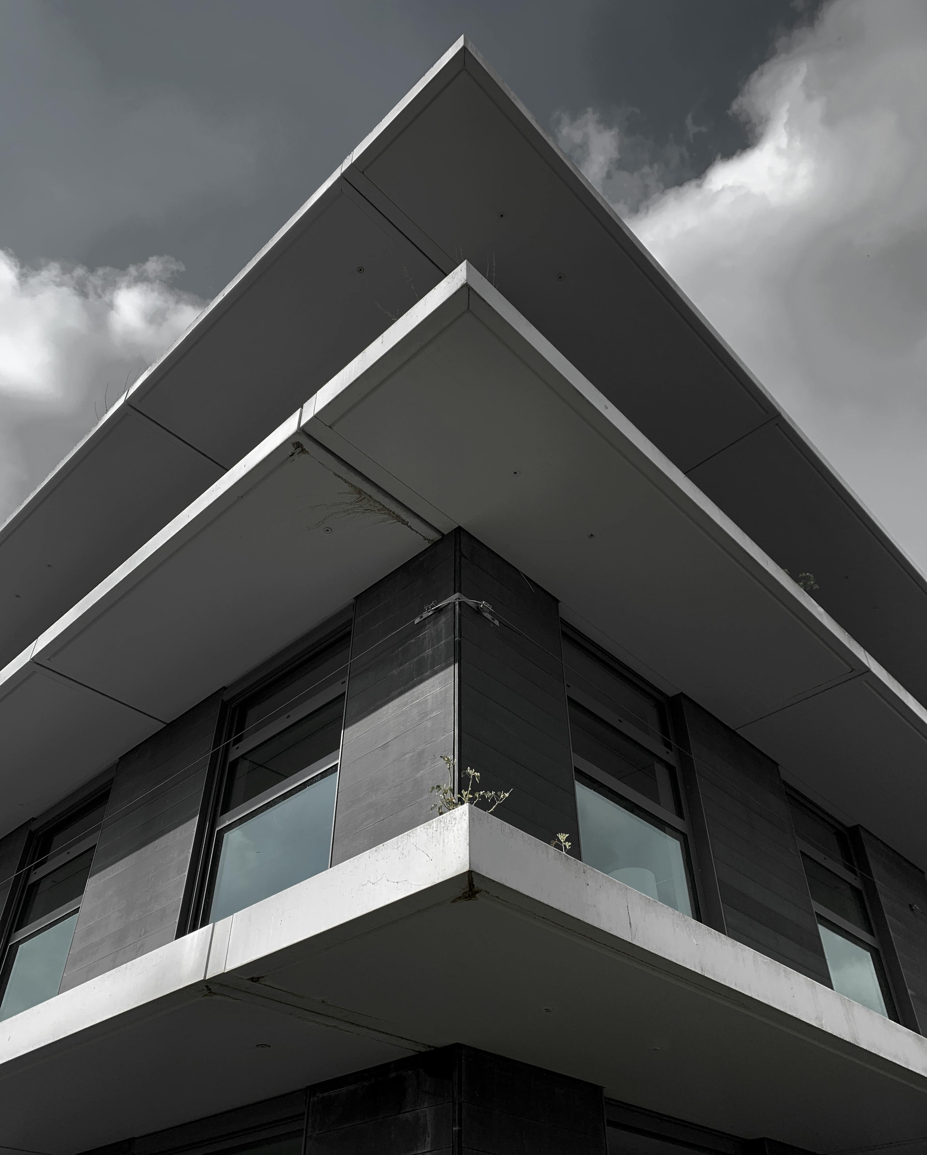 Free A dramatic low-angle view of a modern building with glass windows and geometric lines in grayscale. Stock Photo