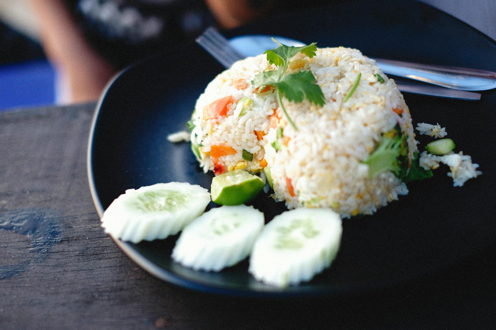 Appetizing fried rice with vegetables garnished with cucumber slices on a black plate.