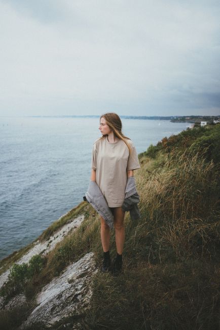 A woman standing on a cliff by the sea, gazing into the distance on a cloudy day.
