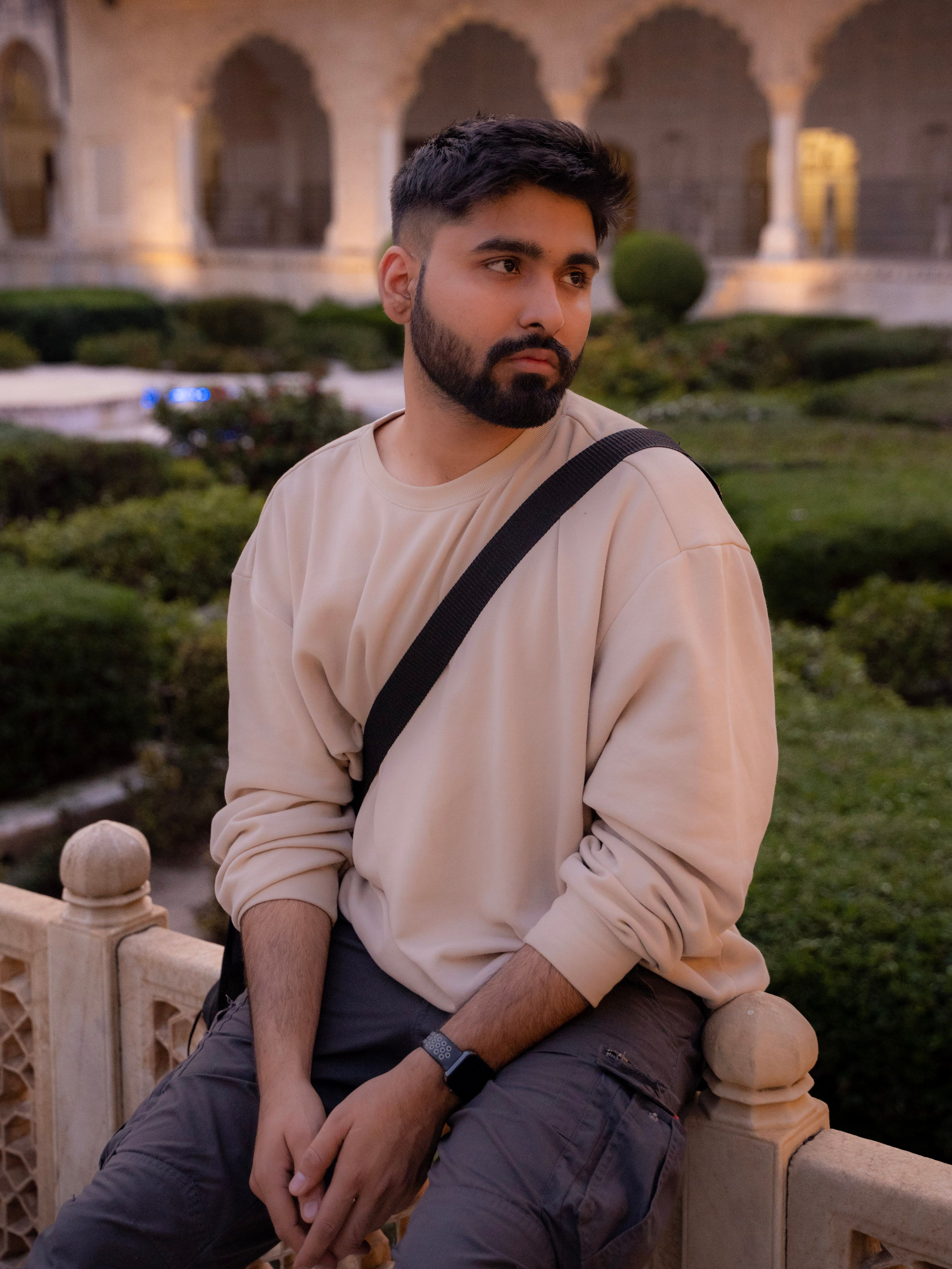 A bearded man in a casual sweater posing thoughtfully in a beautiful historic garden.