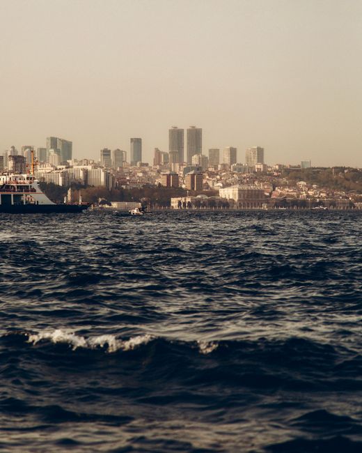 A serene view of a ferry crossing the ocean against a bustling urban skyline.