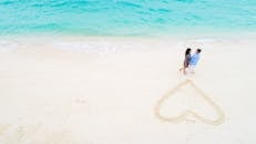 在风景如画的马尔代夫海滩上的一对快乐的夫妇的鸟瞰图与在沙子中画的心