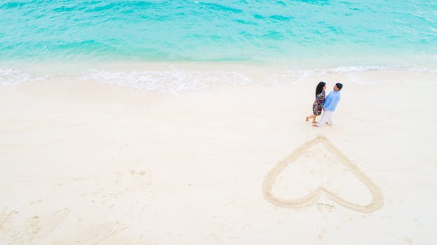 从空中俯瞰，一对幸福的夫妇在风景如画的马尔代夫海滩上，将心形图案画在沙子里