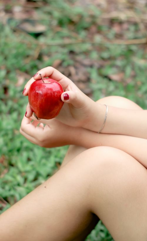 Free A woman holding a red apple while sitting on grass, showcasing healthy lifestyle choices. Stock Photo
