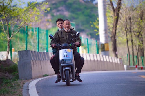 Men Riding a Scooter on the Road