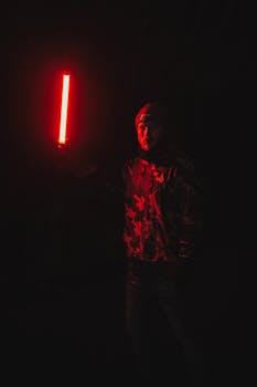 Man in camouflage jacket holding a red light saber in a dark setting, creating a dramatic night scene.