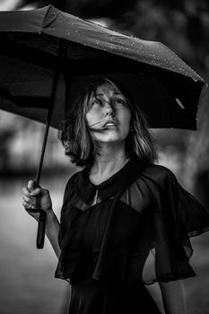 Moody black and white portrait of a woman looking up while holding an umbrella in the rain.