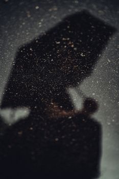Shadowy figure holding an umbrella, reflected on wet pavement at night, creating a mysterious mood.