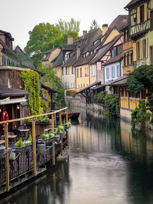 Free Scenic view of a picturesque European canal flanked by historic houses, lush greenery, and vibrant urban life. Stock Photo