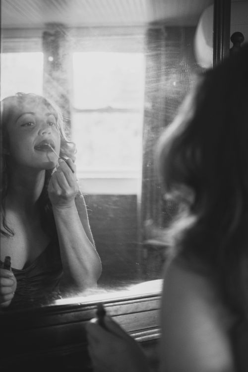 Free A woman elegantly applies lipstick, reflected in a vintage mirror, in black and white. Stock Photo