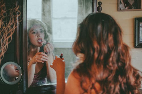 Free A Woman Applying Lipstick while Looking at the Mirror Stock Photo