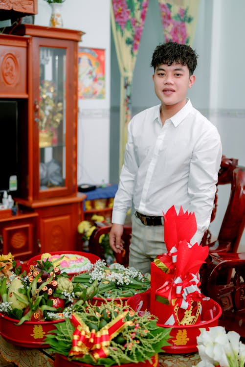 A Man in White Long Sleeves Smiling while Standing Near the Table with Flowers