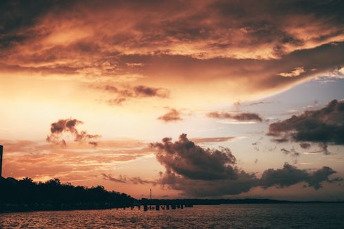 Free Dramatic sunset sky over a tranquil ocean with silhouette of distant trees. Stock Photo