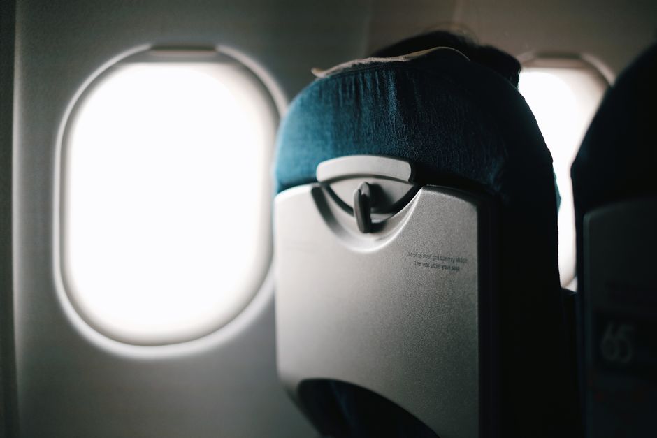 View of an airplane seat with window revealing a bright sky outside.
