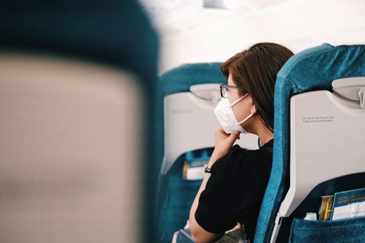 A woman sits on an airplane, wearing a face mask during the flight, representing the new normal of air travel.