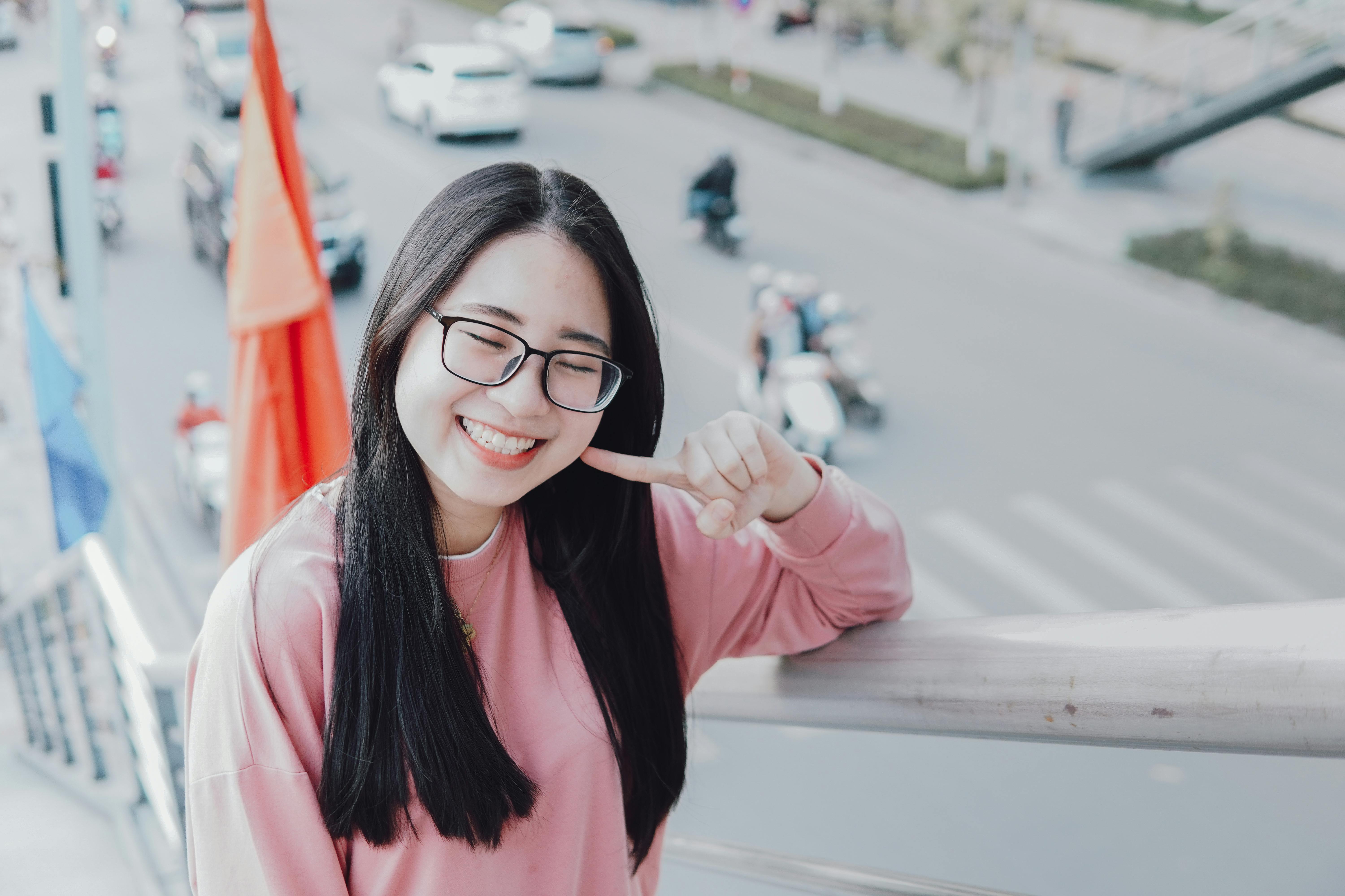 A happy woman in a pink sweater leans on a railing, smiling brightly outdoors.