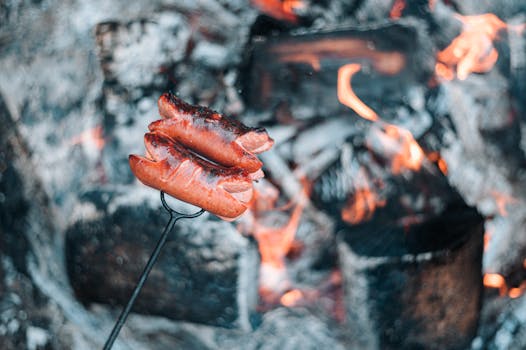 Juicy sausages grilling over open flames on a charcoal barbecue, perfect for outdoor cooking.