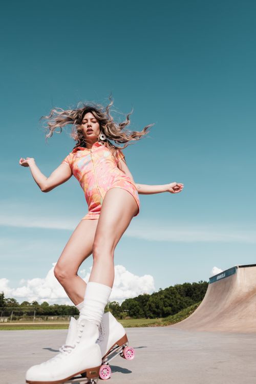 Free Young woman in vibrant outfit roller skating at a skate park under blue skies. Stock Photo