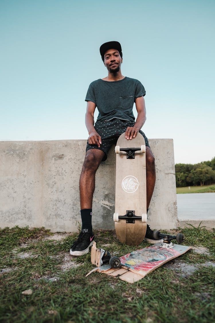 Man In Black Shirt Holding A Skateboard Leaning On A Concrete Wall