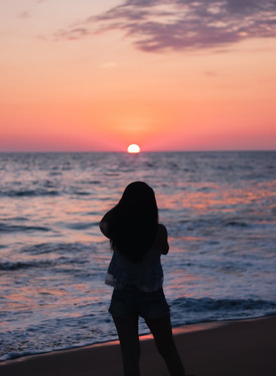 Silhouette of Woman Standing on Seashore during Sunset · Free Stock Photo