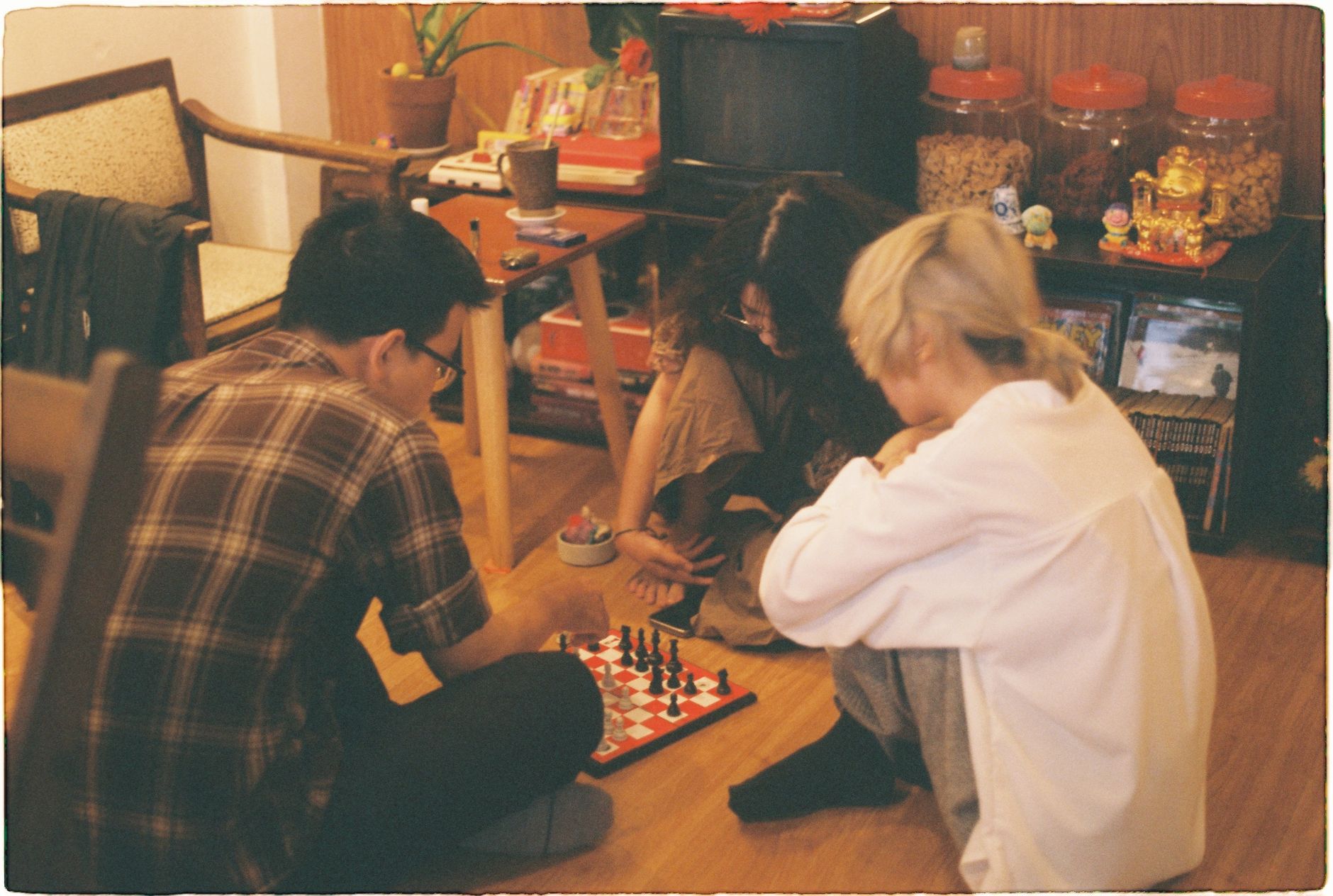Three friends play chess indoors, enjoying a relaxed and intimate moment of strategic gameplay.