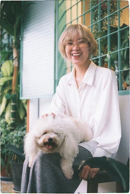 Happy woman with glasses petting a poodle sitting on her lap outside.