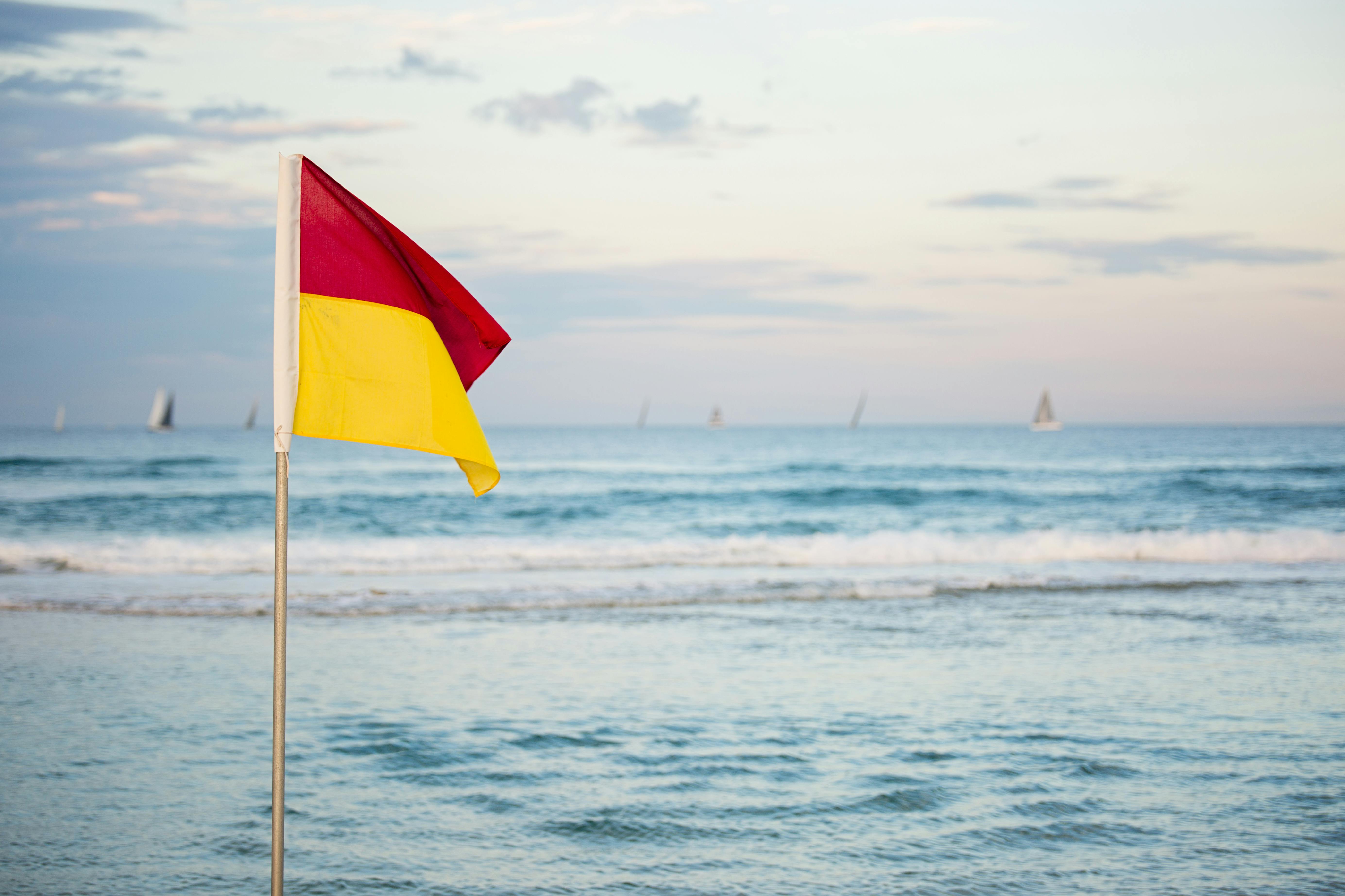 red-and-yellow-flag-standing-near-beach-free-stock-photo