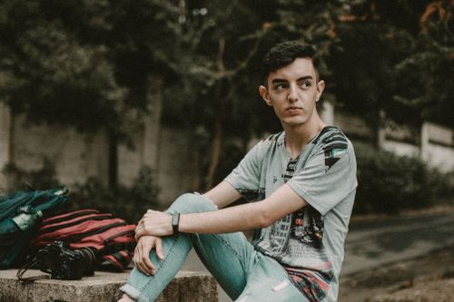 Free Casual young man sitting outdoors in São Paulo, with a camera beside him. Relaxed urban photography vibe. Stock Photo