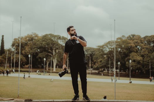 A man with a camera stands in a scenic park in São Paulo, Brazil, surrounded by trees and open space.