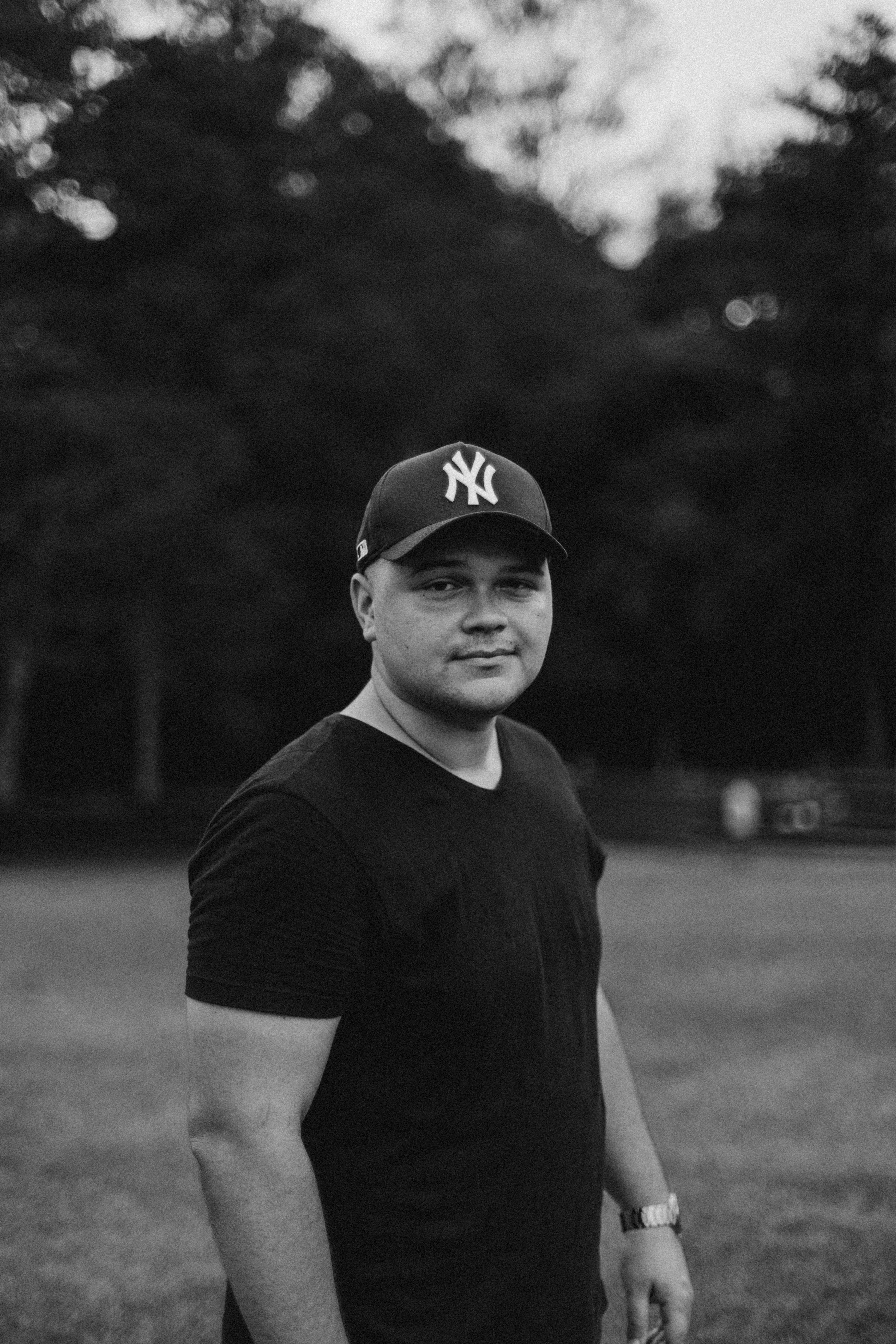 Black and white portrait of a man wearing a cap in a park setting. Moody and classic.