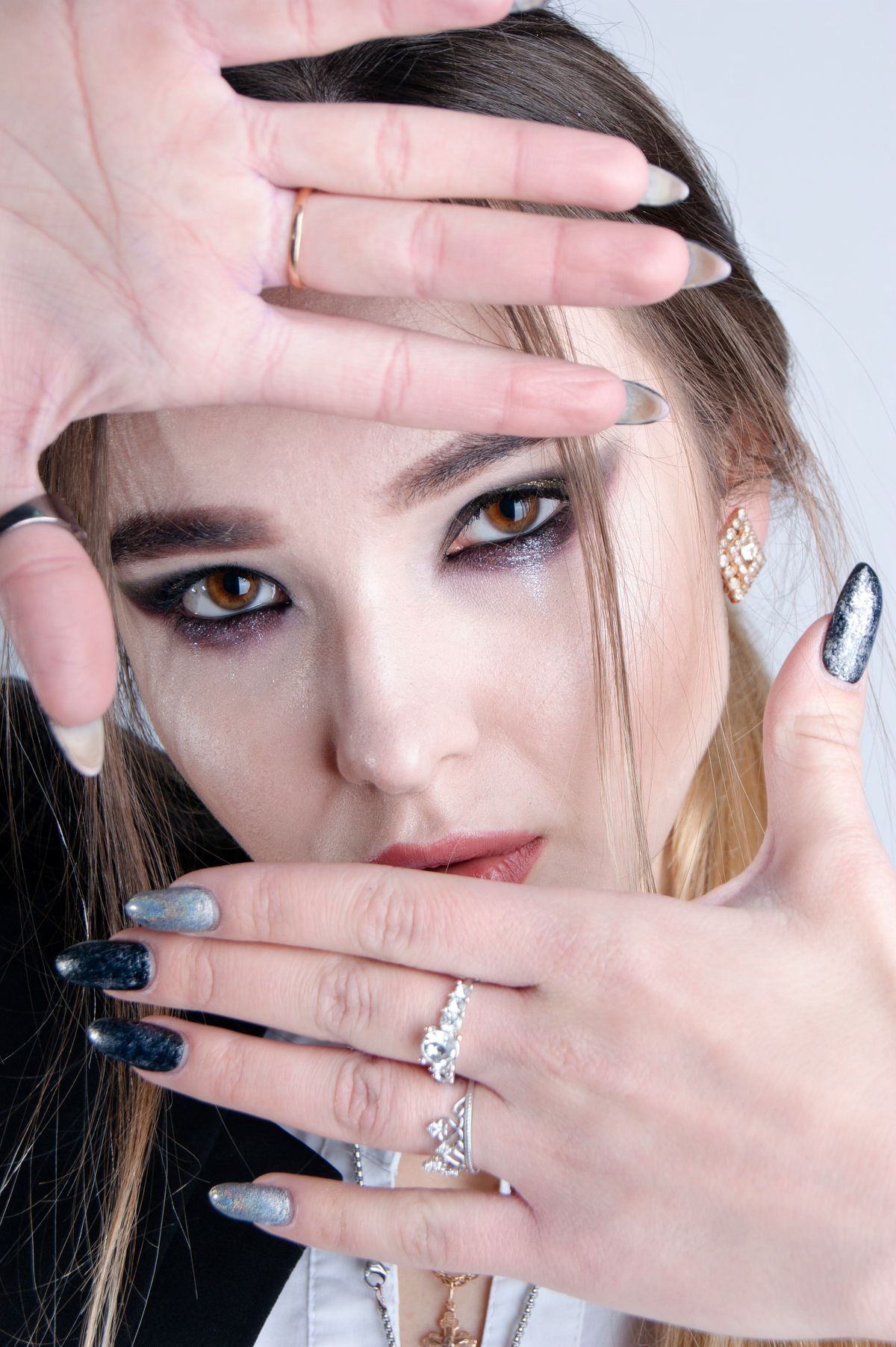 Close-up of a woman with striking makeup and manicure, framed by her hands.