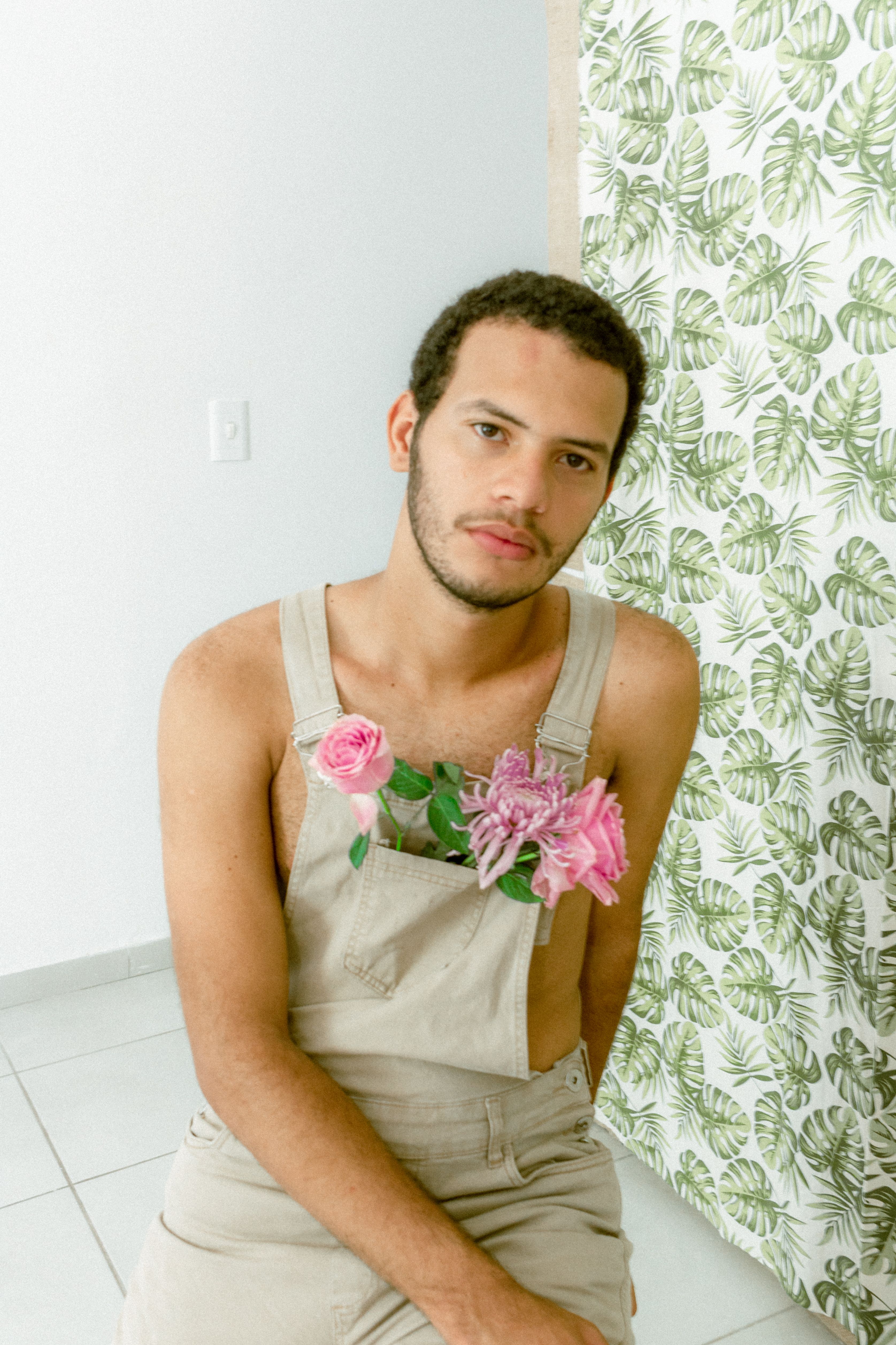 An artistic indoor portrait of a man with flowers in overalls, showcasing creativity.