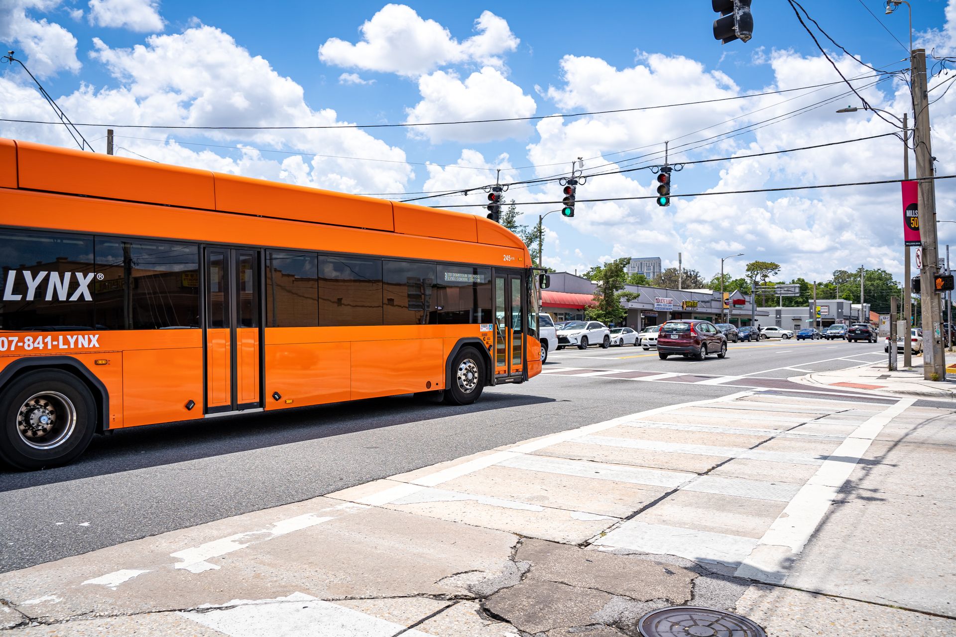Orange Lynx bus traveling on a busy street in Orlando, FL, with clear skies and traffic lights.