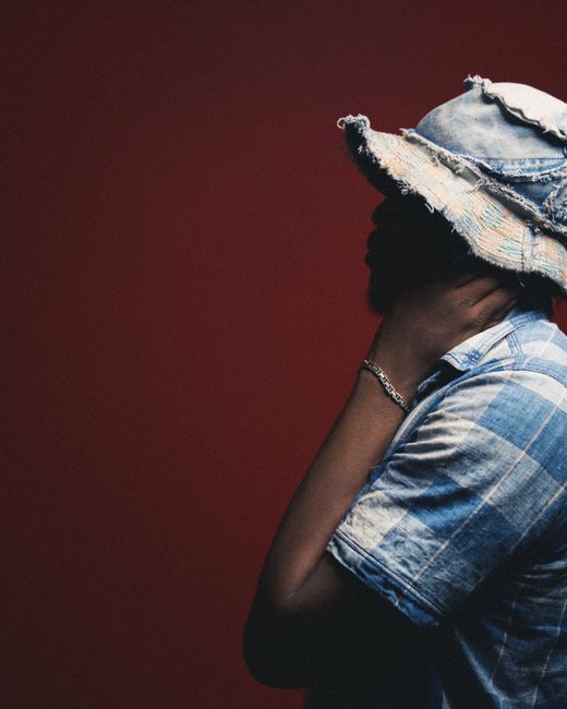 Side view of a stylish man in a denim shirt and hat against a red background.