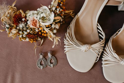 Free Wedding accessories including sandals, earrings, and a floral bouquet in a stylish flat lay. Stock Photo