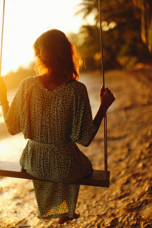 Free A woman in a dress sits on a swing by the seashore, enjoying the sunset. Stock Photo