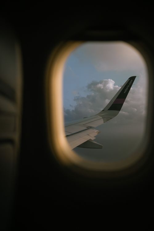 Free A serene view of an airplane wing during flight, captured through a window with clouds in the sky. Stock Photo