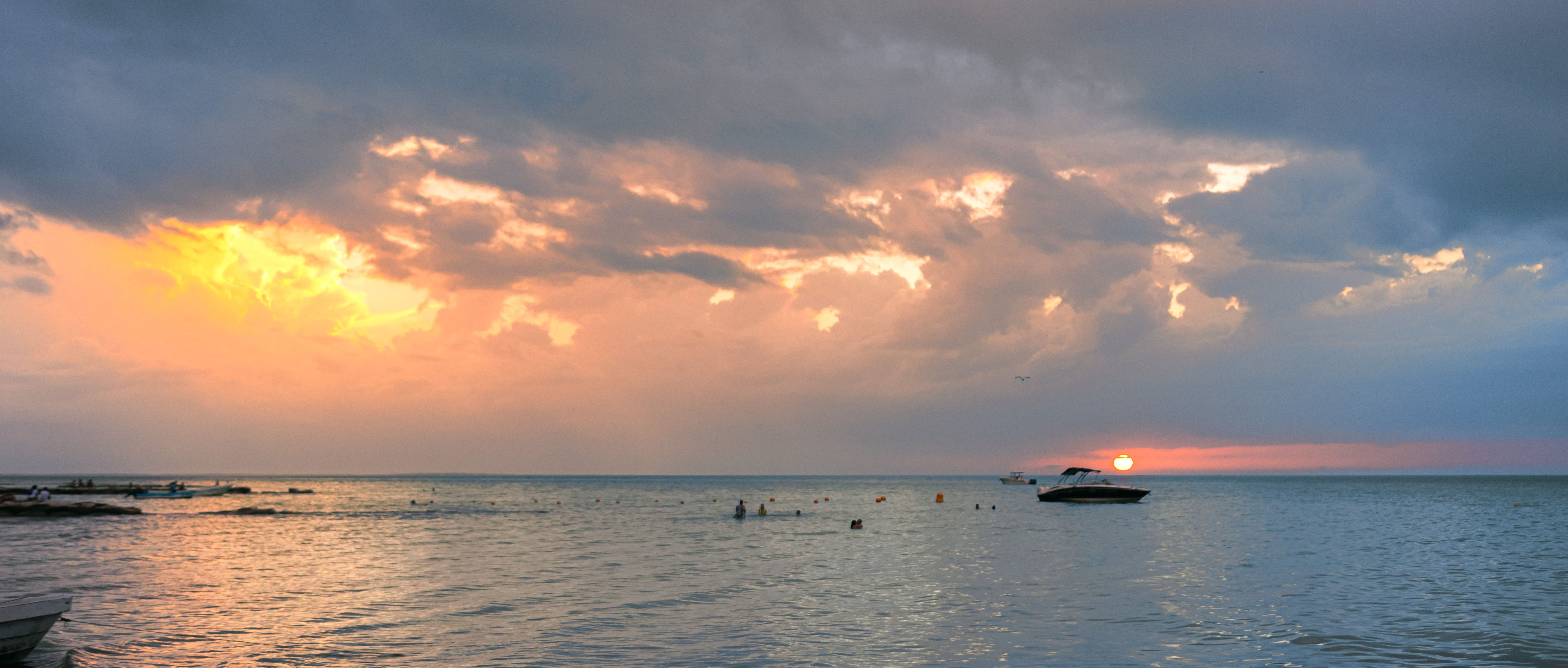 A serene sunset view of the ocean at Holbox Island, Mexico, with boats and distant swimmers. A serene sunset view of the ocean at Holbox Island, Mexico, with boats and distant swimmers.