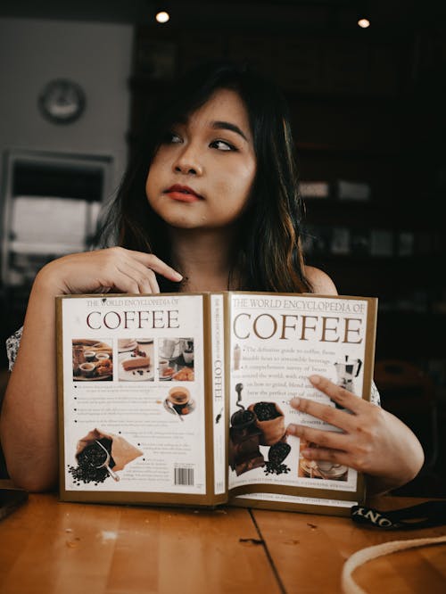Free A Woman Holding a Book About Coffee Stock Photo