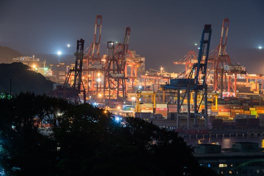 Illuminated port at night with large cranes and shipping containers, showcasing industrial logistics.