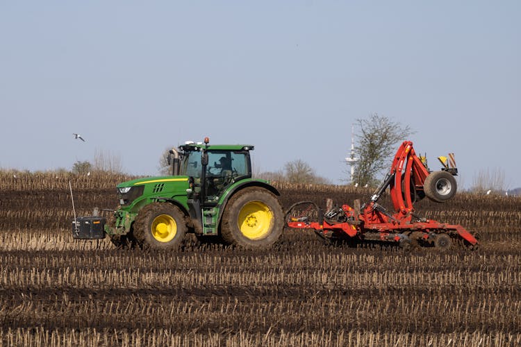 Green Tractor Plowing On The Field