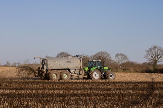A Tractor Fertilizing Brown Field
